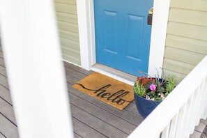 A blue door with a brown doormat that reads "hello" and a potted plant with flowers. - House on cul-de-sac  (Staunton)