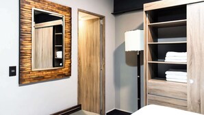 Habitación de hotel con un panel de pared de madera, un armario con estantes y una lámpara de noche.