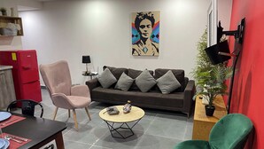 En moderne stue med sofa, to stole, sofabord og et rødt køleskab.