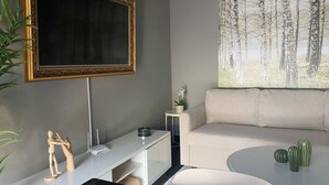 A modern living room with a flat-screen TV, a sofa, a coffee table, and a painting of a forest. - Excelente Departamento a una cuadra del Ángel (Ciudad de México)