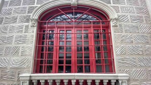 A building facade with a red-framed window, stone wall texture, and a balustrade. - Excelente Departamento a una cuadra del Ángel (Ciudad de México)