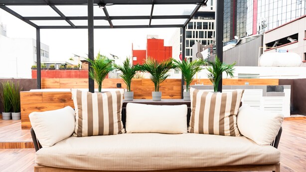 Un espacio al aire libre moderno con un banco de madera, cojines a rayas y plantas en macetas.