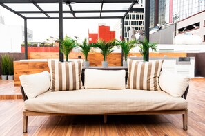 Un espacio al aire libre moderno con un banco de madera, cojines a rayas y plantas en macetas.