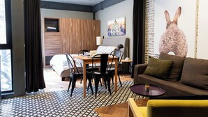 A modern hotel room with a wooden wardrobe, a dining table with chairs, a sofa, a large window with curtains, and a wall with a rabbit mural. - Lujoso Departamento muy Amplio en la condesa (Ciudad de México)