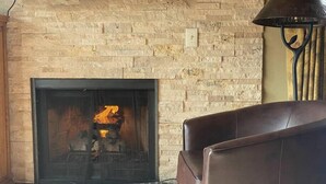 A fireplace with a fire, a brown leather sofa, and a patterned rug in a room with a brick wall. - Beautiful view by the creek, close to Vail Village (Vail)