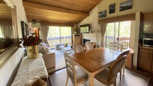 A cozy cabin interior with a wooden dining table, white chairs, a fireplace, and a stone wall. - Beautiful view by the creek, close to Vail Village (Vail)