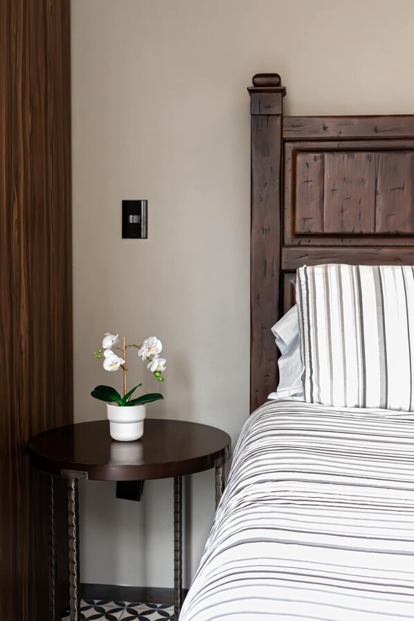 Hotelkamer met een houten hoofdeinde, een gestreept beddegoed, een klein rond tafeltje met een potorkidee en een zwarte schakelaar aan de muur.