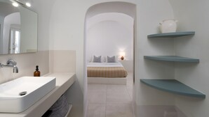Een moderne badkamer met een wit wastafel, een spiegel en een bed op de achtergrond.
