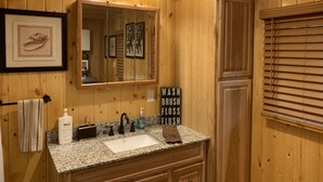 Ein Badezimmer aus Holz mit Waschbecken, Spiegel und drei Pendelleuchten.
