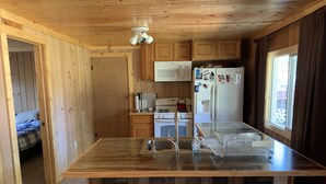 Eine kleine Küche mit Holzausstattung, einer eingebauten Mikrowelle, einem Kühlschrank und einem Fenster mit Vorhängen.