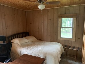 Une chambre dans une cabane en bois, comprenant un lit, un bureau, une chaise, un ventilateur de plafond et une fenêtre.