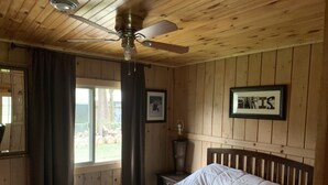 Ein Schlafzimmer mit Holzboden, einem Bett, einem Nachttisch, einem gerahmten Bild und einem Fenster mit Vorhängen.
