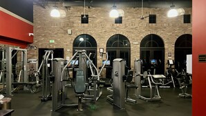Un gimnasio con diversas máquinas de ejercicio, una pared de ladrillo y arcos.