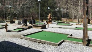 Un parcours de minigolf doté de plusieurs zones d’entraînement au putting, entouré de gravier et d’arbres.