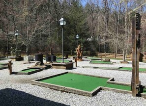 A miniature golf course with multiple green putting areas, surrounded by gravel and trees.