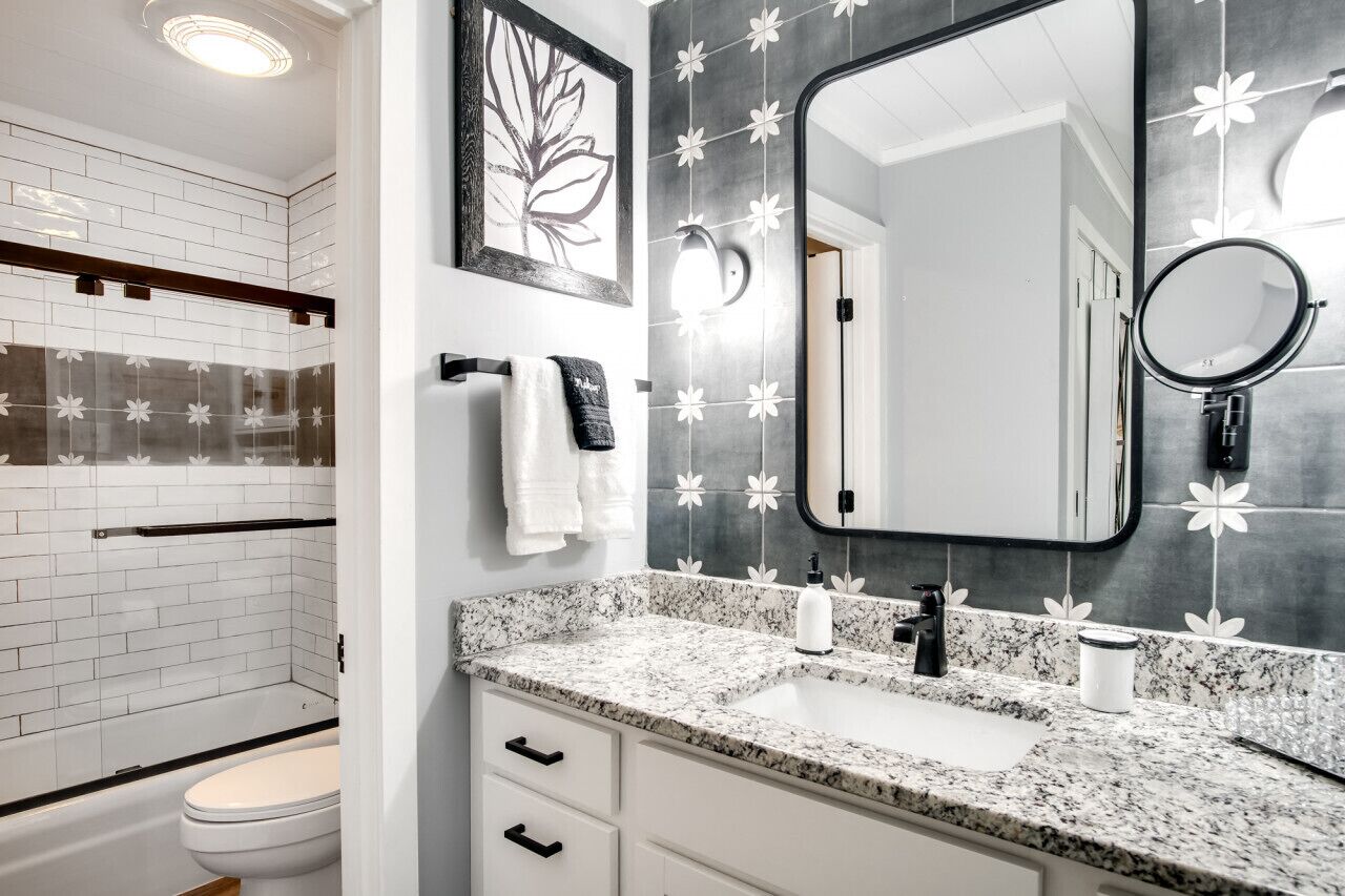 Une salle de bain moderne avec des toilettes blanches, un lavabo doté d’un plan de travail en marbre et un grand miroir.
