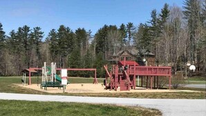 Une aire de jeux avec une structure rouge, un toboggan vert et un banc.