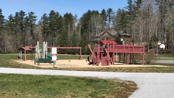 Une aire de jeux avec une structure rouge, un toboggan vert et un banc.