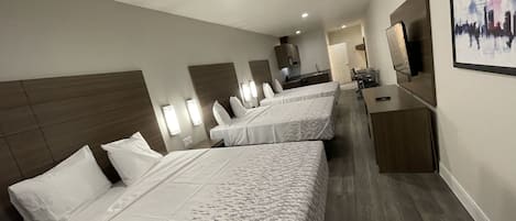 A hotel room with three beds, a desk, a chair, a TV, and a painting on the wall.