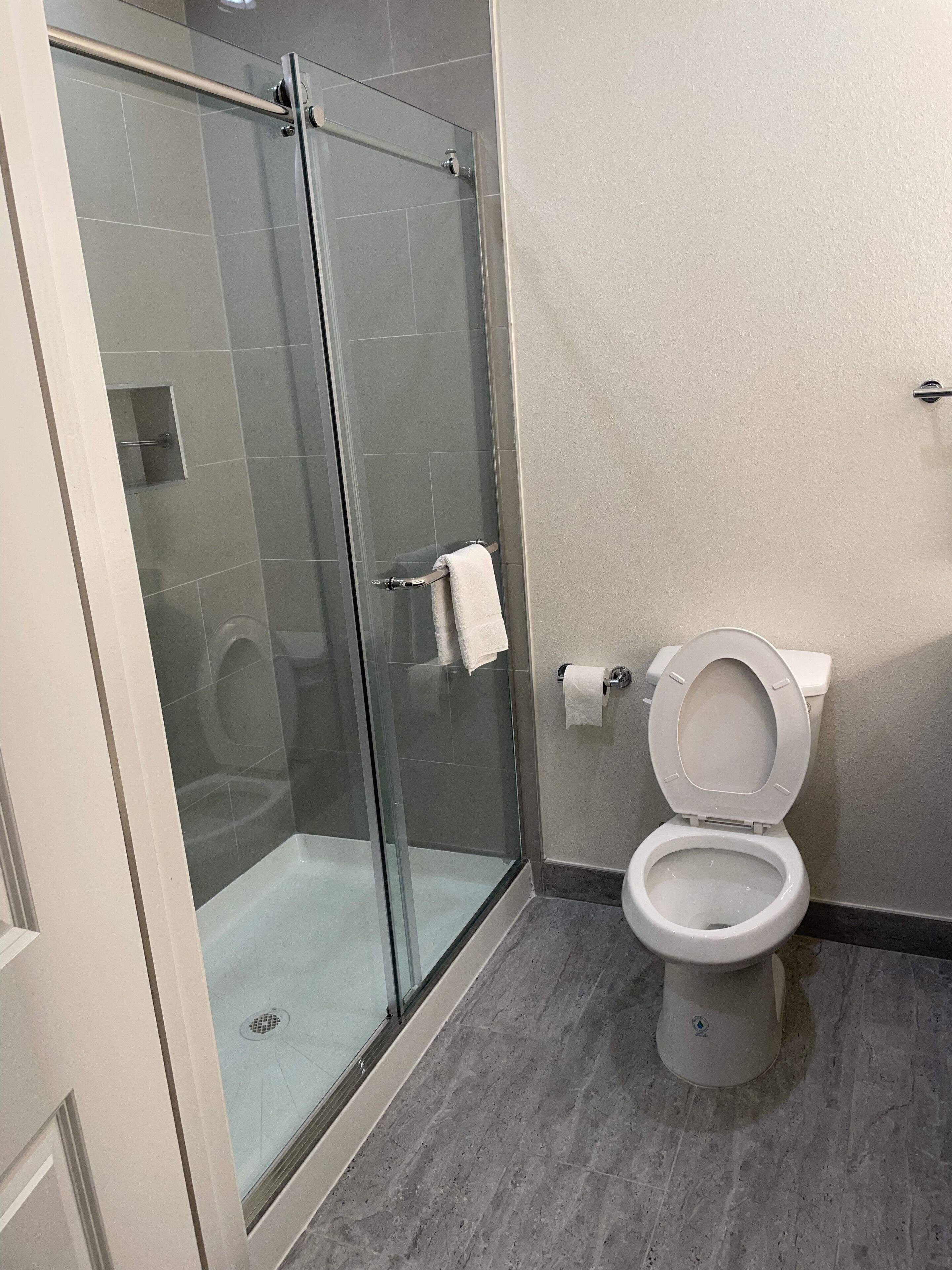 Un baño moderno con ducha de vidrio, inodoro y piso de mármol.