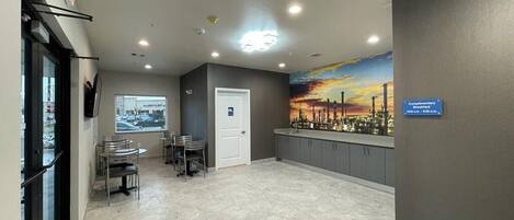 A hotel lobby with a cityscape mural, a reception desk, and a seating area with tables and chairs.