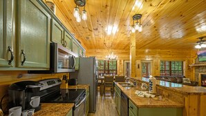 Interior de una cabaña de madera con cocina, mostradores de granito, cafetera y refrigerador.