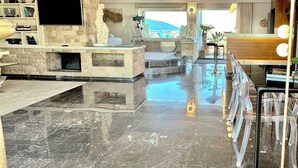 A spacious living area with a marble floor, a stone fireplace, a mounted TV, and a bar area with a view of the outdoors. - One 360 Skyline Athens - Penthouse Suite with private Infinity Jacuzzi  (Athens)