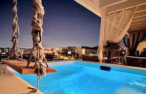 An indoor swimming pool with ropes, a view of a cityscape at dusk, and cacti in the background. - One 360 Skyline Athens - Penthouse Suite with private Infinity Jacuzzi  (Athens)
