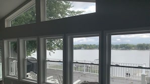 Une pièce dotée de grandes fenêtres donnant sur un lac, d’une terrasse et d’une clôture blanche.