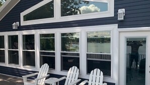 Une maison dotée d’un porche abrité, de chaises Adirondack blanches et de grandes fenêtres.