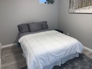 Een slaapkamer met een bed, grijze wanden en een klein raam.