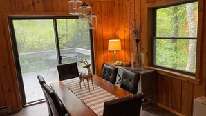 Un espace repas comprenant une table en bois, des chaises et une vue sur l’extérieur grâce à de grandes fenêtres.