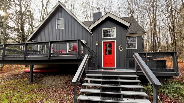 Une maison à deux étages avec une porte rouge, un balcon avec des chaises rouges et le chiffre « 8 » sur le côté.