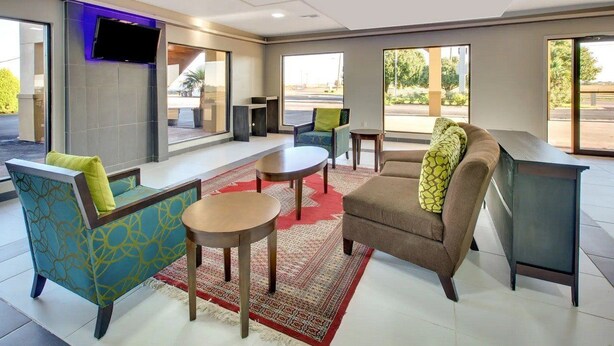 A modern hotel lobby with seating arrangements, a flat-screen TV mounted on the wall, and large windows providing views of the outdoors. - Baymont by Wyndham Terrell (Terrell)