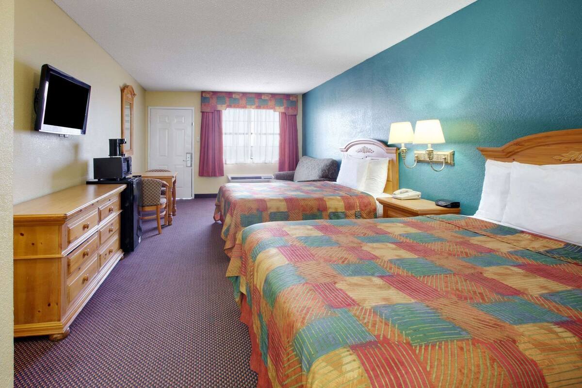 A hotel room with two beds, a desk with a TV, a chair, a dresser, and a window with curtains.