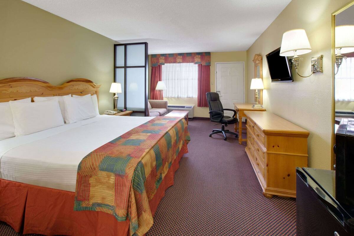 A hotel room with a large bed, a desk, a chair, a dresser, a television, and a window with curtains.