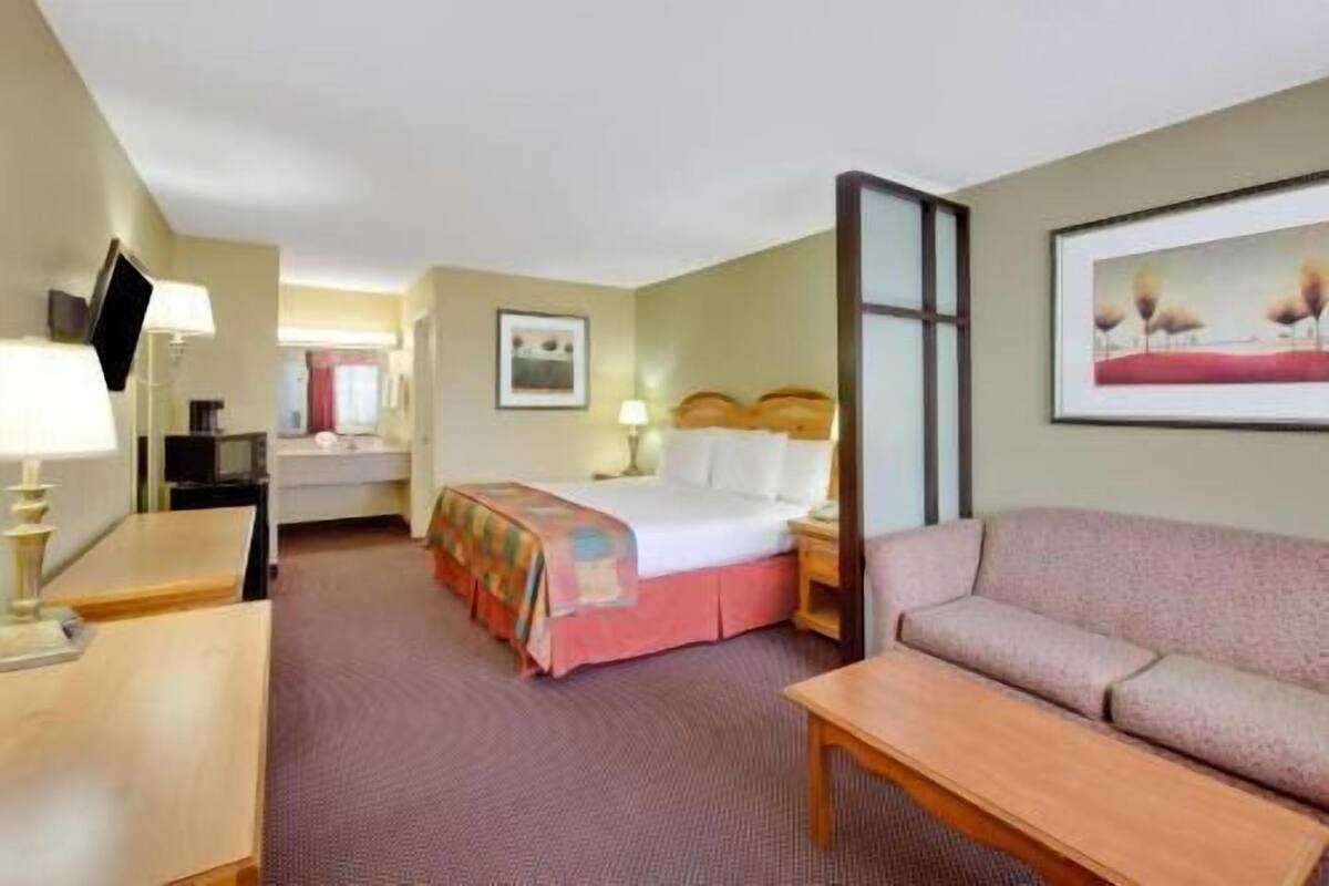 A hotel room with a bed, a sofa, a desk with a lamp, a television, and a framed picture on the wall.