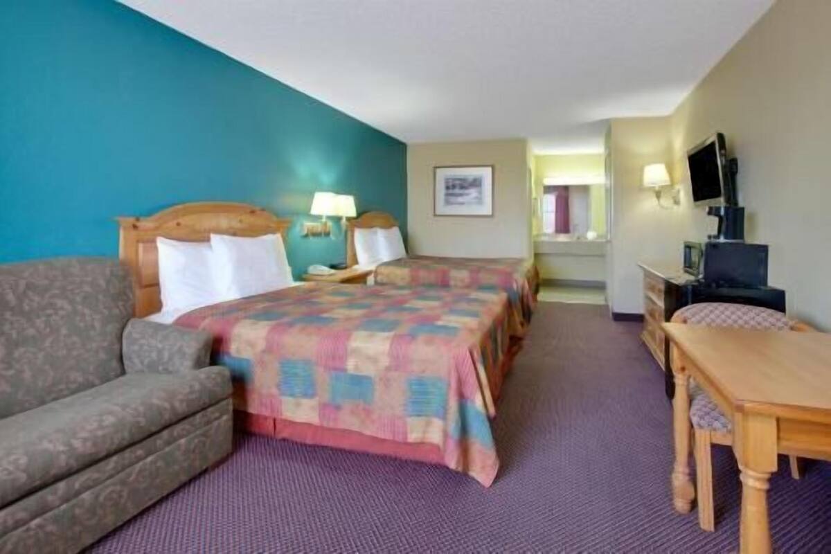 A hotel room with two beds, a sofa, a desk, and a television.