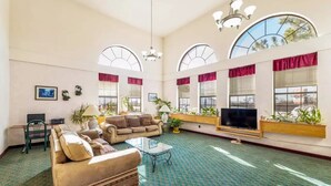 A spacious living room with a large sofa, a coffee table, and a TV. There are arched windows with red curtains and potted plants. - Rodeway Inn Decatur (Decatur)