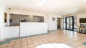 A reception area with a counter, a door with an exit sign, and a magazine rack. - Rodeway Inn Decatur (Decatur)