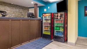 Un espace d’accueil comprenant un comptoir, un mur en pierre et deux distributeurs de boissons réfrigérées de la marque Coca-Cola.