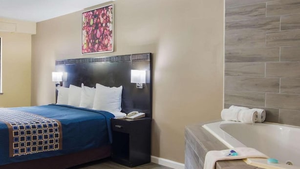 Une chambre d’hôtel comprenant un lit, une table de chevet, une lampe, des œuvres d’art et une salle de bain avec une baignoire et des serviettes.