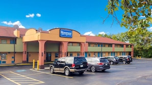 Un motel avec une enseigne indiquant « Rodeway Inn & Suites », comprenant un parking avec plusieurs voitures et un bâtiment doté d’un toit rouge et de murs de couleur beige.