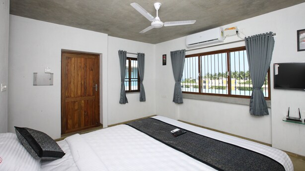 A bedroom with a bed, a ceiling fan, a window with curtains, an air conditioning unit, and a wooden door. - Hotel Du Palais (Vanur)