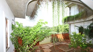 A courtyard with a stone pathway, green plants, and a white building with a curved roof. - Hotel Du Palais (Vanur)