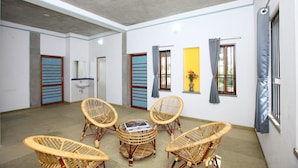 A spacious room with a ceiling fan, a round table with chairs, and a window with curtains. - Hotel Du Palais (Vanur)