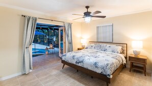 Un dormitori amb un llit, dues làmpades de nit, un ventilador de sostre i vista a una zona de piscina exterior.