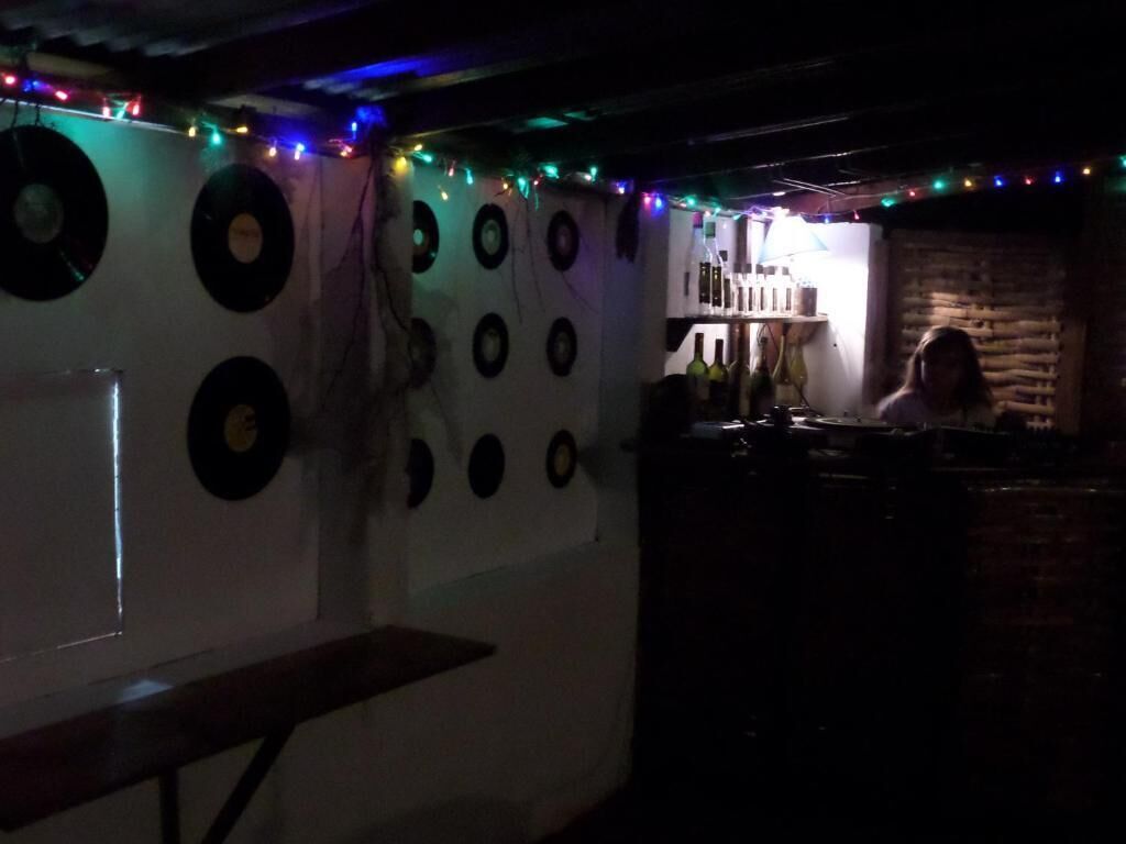 Una habitación tenuemente iluminada con discos de vinilo en la pared, un banco de madera y una pared de ladrillo al fondo.
