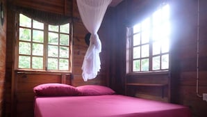 A wooden cabin room with a bed, two windows, and a mosquito net. - La Familia Guesthouse (Long Bay)