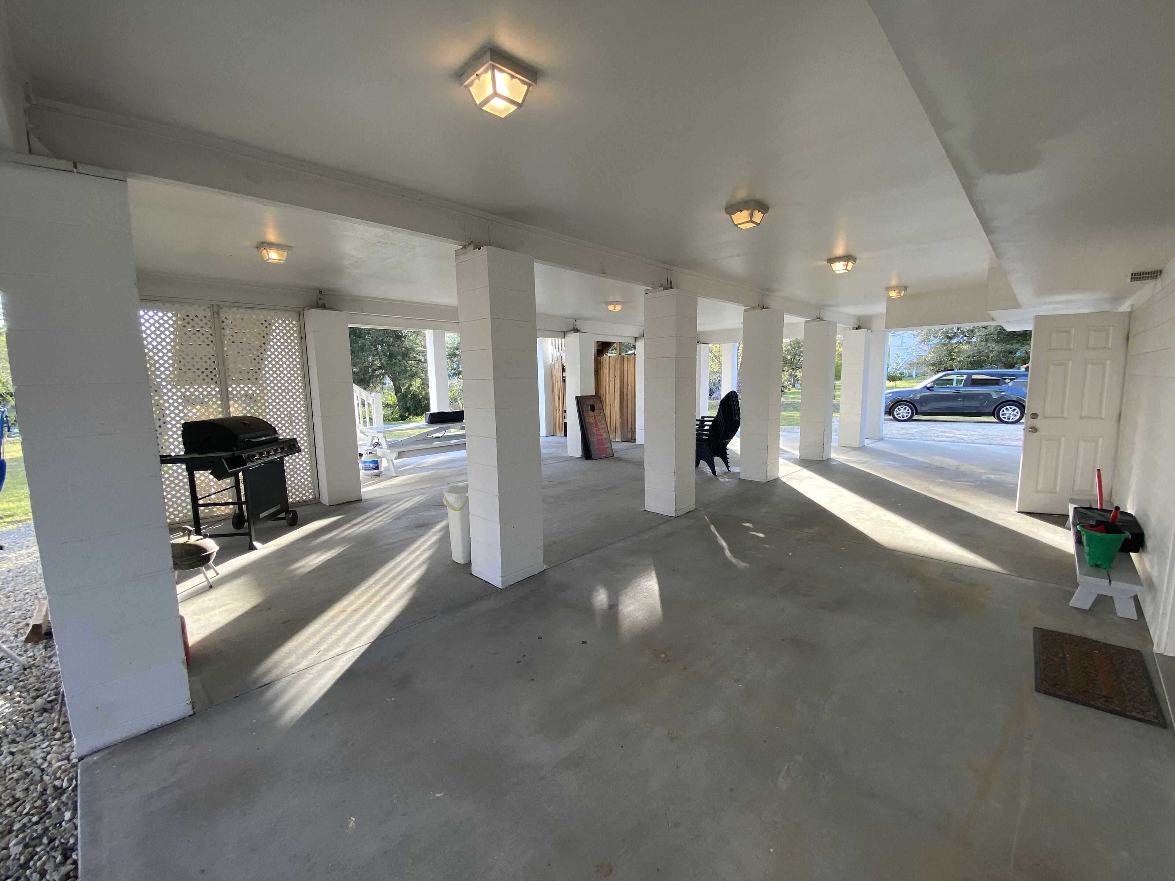 A covered outdoor area with concrete flooring, white pillars, and overhead lighting.